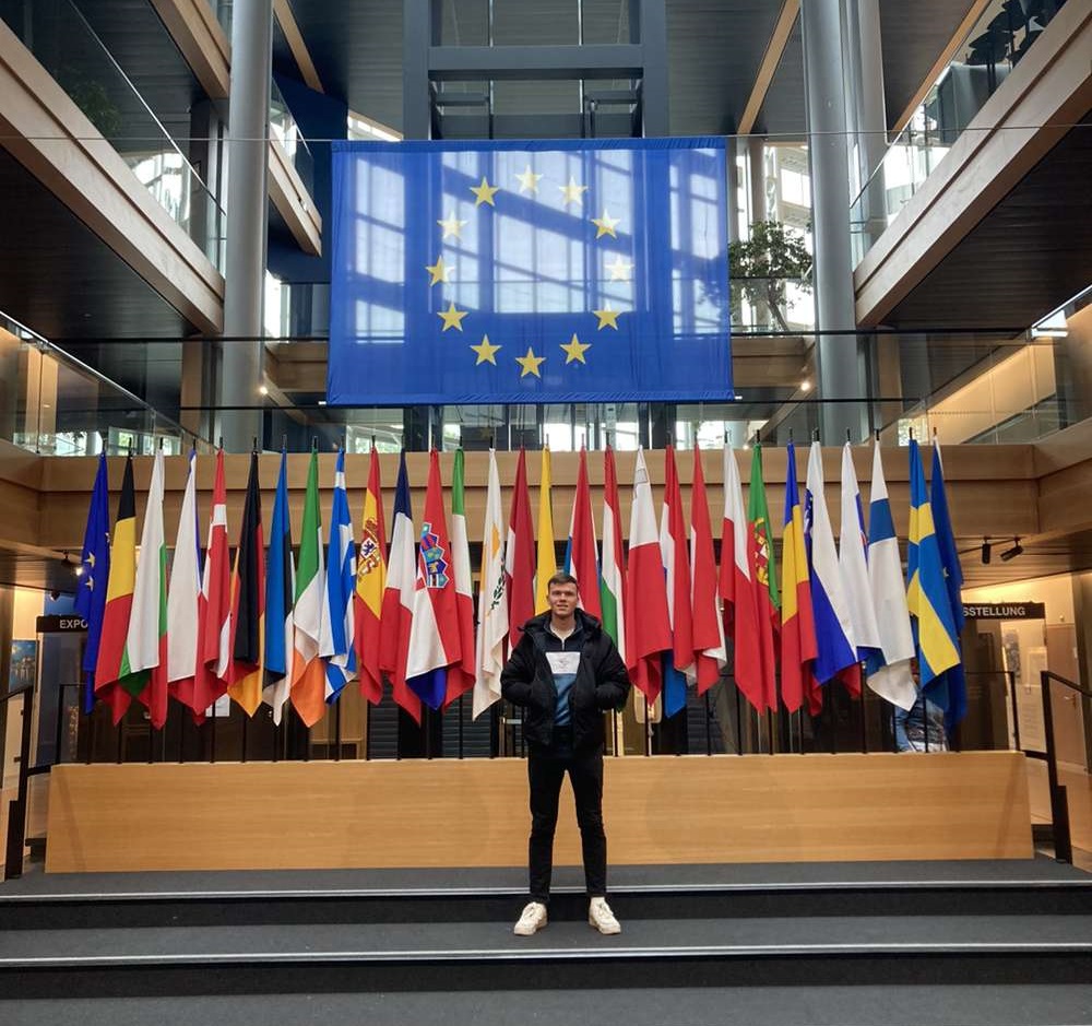 Henley Business School student Aled standing in front flags in Strasbourg Parliament building.