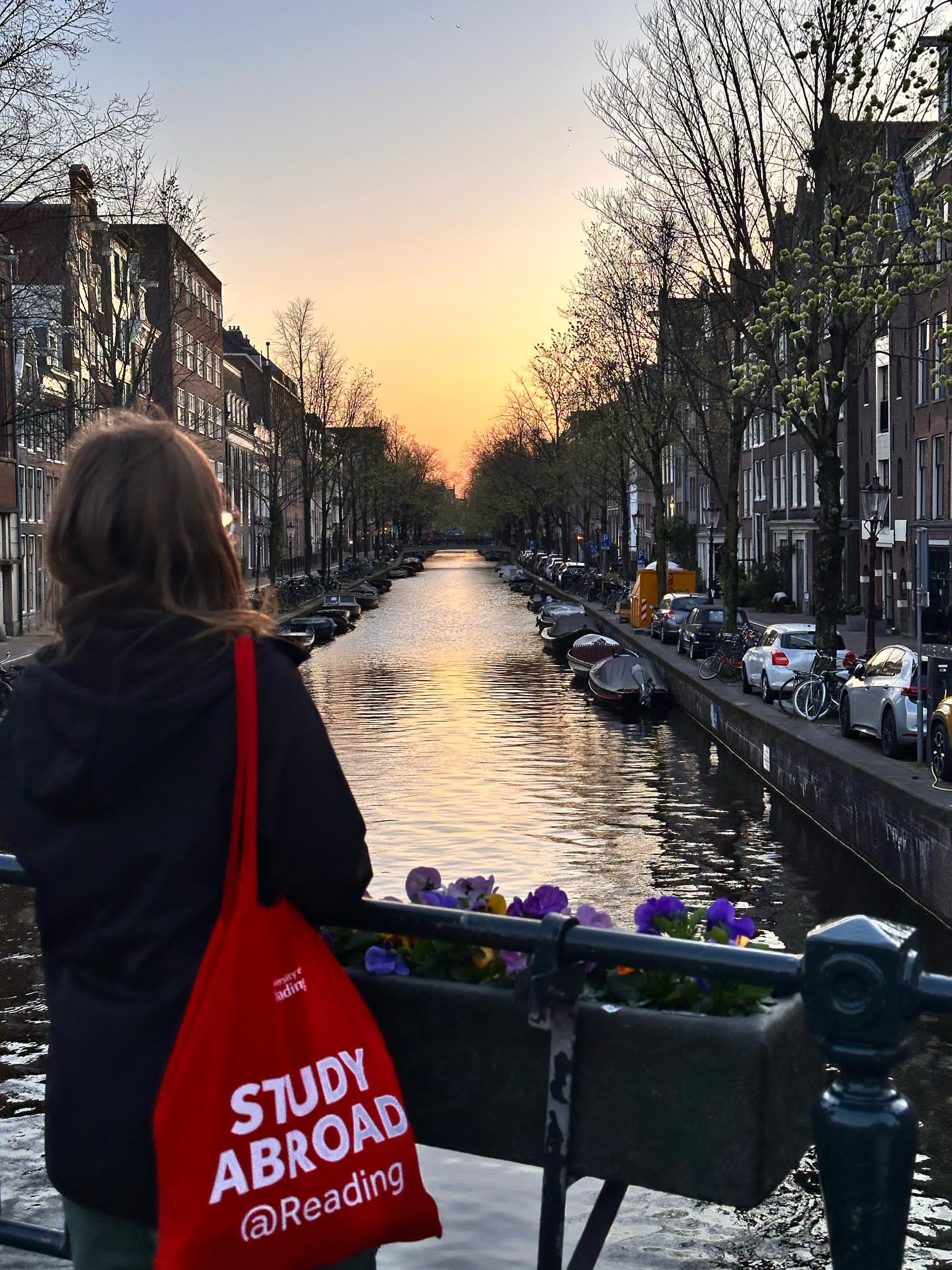 A person with a red tote bag over their shoulder looking out over a canal.